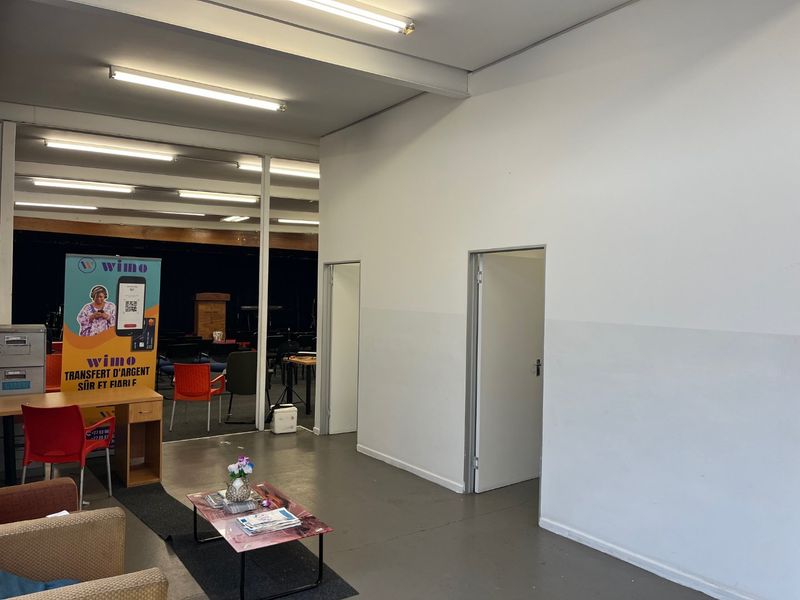 Open plan commercial or multi-purpose space featuring painted concrete floors and fluorescent lighting, with access to adjacent rooms via internal doorways.