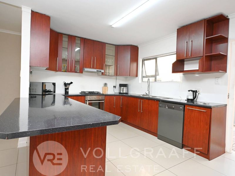 A functional kitchen featuring dark wood cabinetry, granite countertops, a gas hob, and tiled flooring, offering a practical layout for daily cooking.
