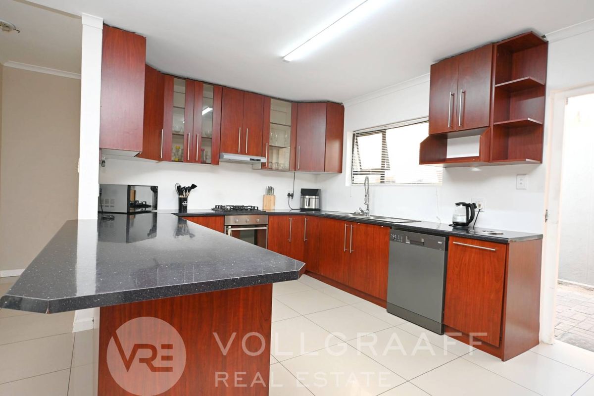 A functional kitchen featuring dark wood cabinetry, granite countertops, a gas hob, and tiled flooring, offering a practical layout for daily cooking.