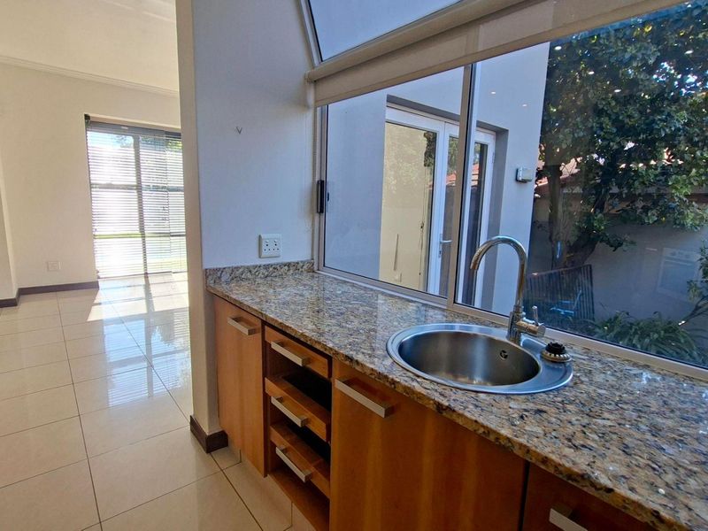 A bright kitchen area featuring granite countertops, wooden cabinetry, and a stainless steel sink, overlooking a private outdoor space through a large window.