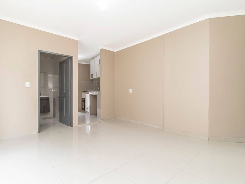An open-plan living area featuring neutral walls, tiled flooring, and a compact kitchen with built-in cabinetry and appliances.