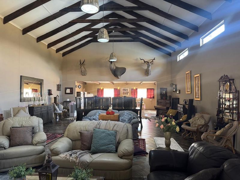Spacious open-plan living area featuring high vaulted ceilings with exposed timber trusses, tiled flooring, and abundant natural light from clerestory windows.