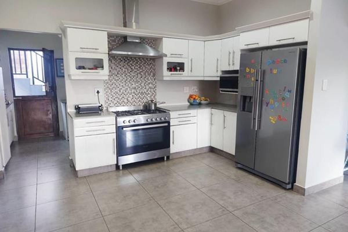 A functional kitchen featuring white cabinetry, a stainless steel gas stove with extractor fan, mosaic backsplash, and neutral tiled flooring.
