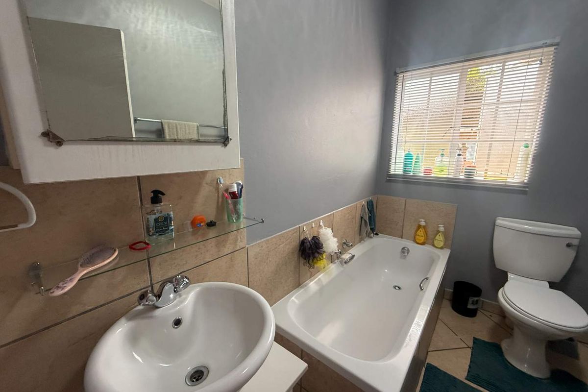 A functional bathroom featuring a built-in bathtub, pedestal sink, wall-mounted mirror, and a window with fitted blinds.