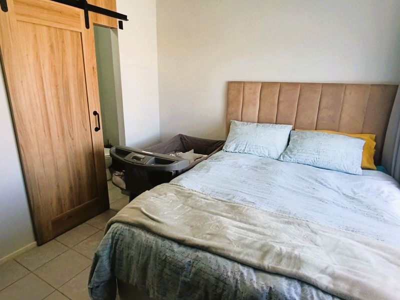 A bedroom featuring a sliding wooden barn door leading to an en-suite bathroom and tiled flooring.