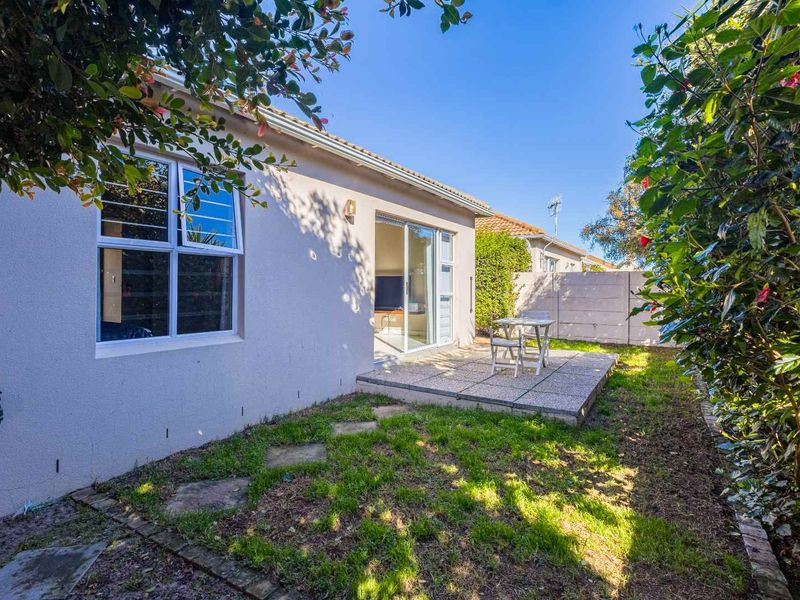 Rear exterior view featuring a paved patio area, sliding glass doors, and a small garden space enclosed by a boundary wall.