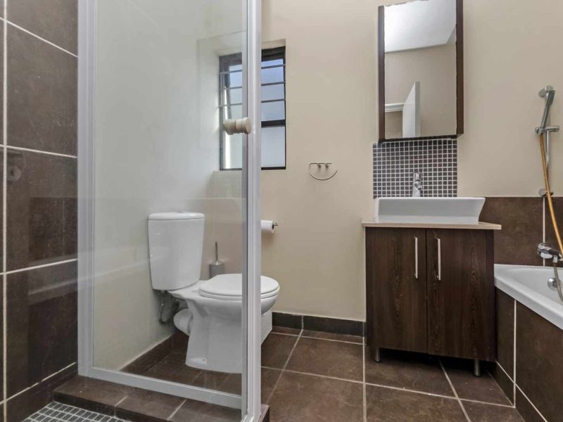 A functional bathroom featuring a shower enclosure, bathtub, vanity cabinet with vessel sink, and wall-mounted mirror cabinet with neutral tiled finishes.