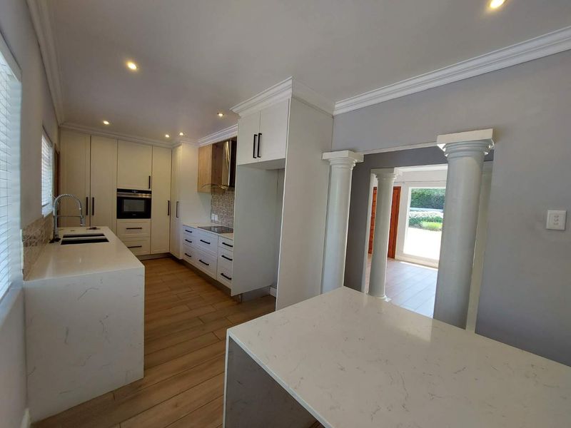 Modern kitchen featuring sleek white cabinetry, stone countertops, integrated appliances, and decorative columns leading to an adjacent living space.