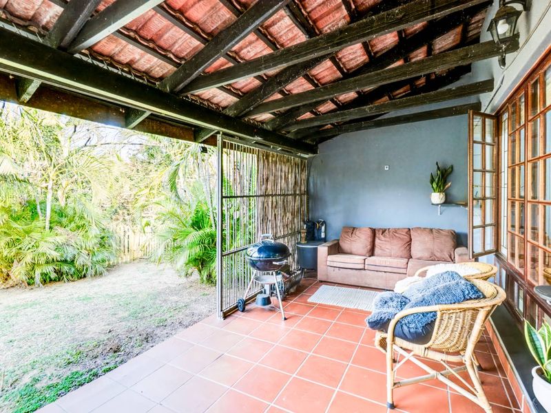 Covered patio area featuring terracotta floor tiles, exposed timber beam ceiling, and direct access to the garden.