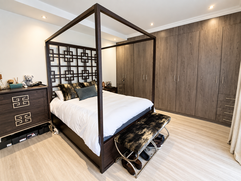 A well-maintained bedroom featuring extensive built-in wooden wardrobes, recessed ceiling lighting, and light-toned laminate flooring.