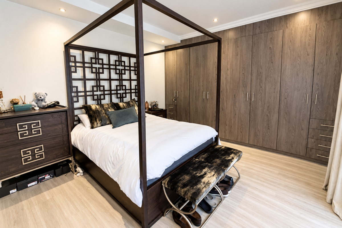 A well-maintained bedroom featuring extensive built-in wooden wardrobes, recessed ceiling lighting, and light-toned laminate flooring.