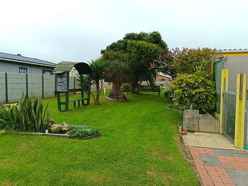 A well-maintained residential garden featuring a lush lawn, mature trees, paved pathways, and secure boundary walling.