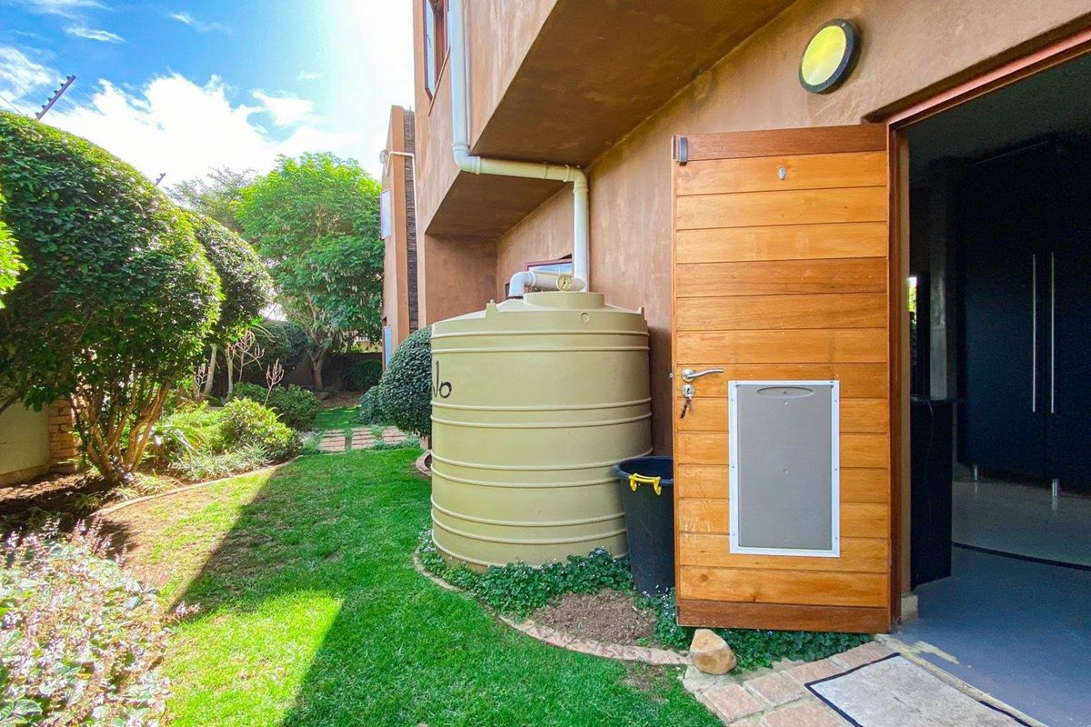 Exterior view of the rear garden featuring a water storage tank, established landscaping, and a wooden door with an integrated pet flap.