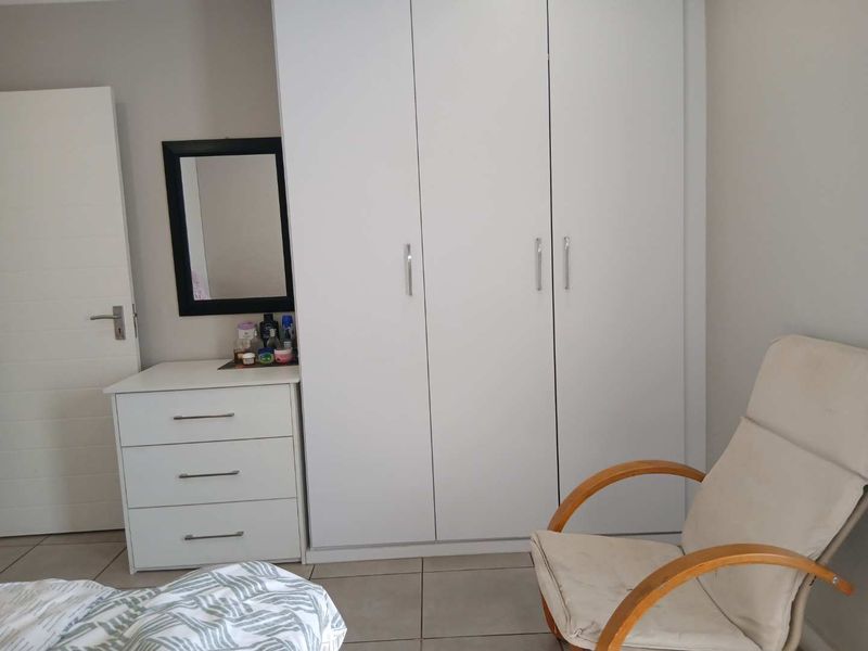 A bedroom featuring neutral tiled flooring and a large white built-in wardrobe providing ample storage space.