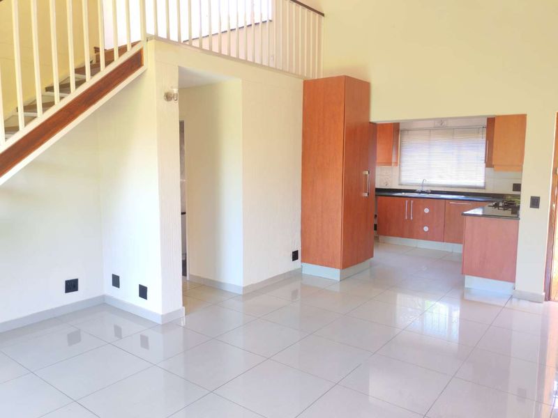 Open-plan living area featuring a staircase and a functional kitchen with built-in cabinetry and granite countertops.