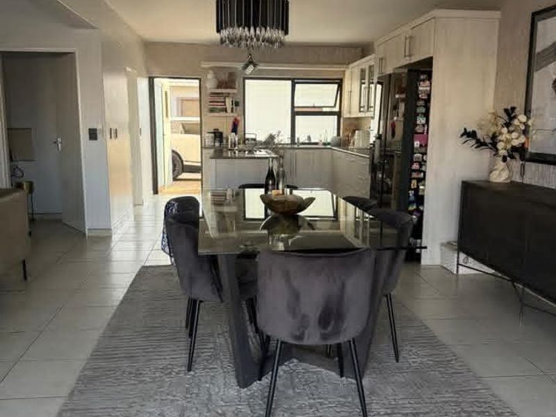 An open-plan dining and kitchen area featuring tiled flooring, modern cabinetry, and a central pendant light fixture, creating a functional and connected living space.
