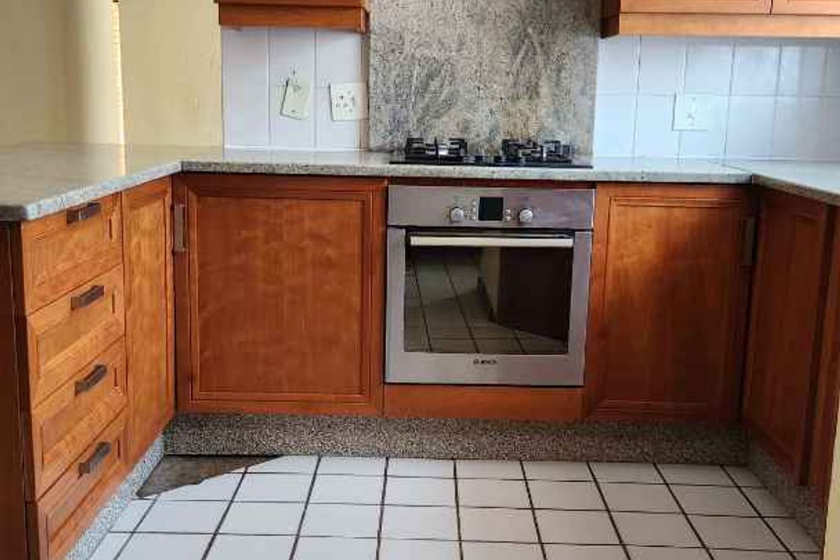 A functional kitchen featuring wooden cabinetry, granite countertops, a built-in oven, gas hob, and stainless steel extractor fan with tiled flooring.