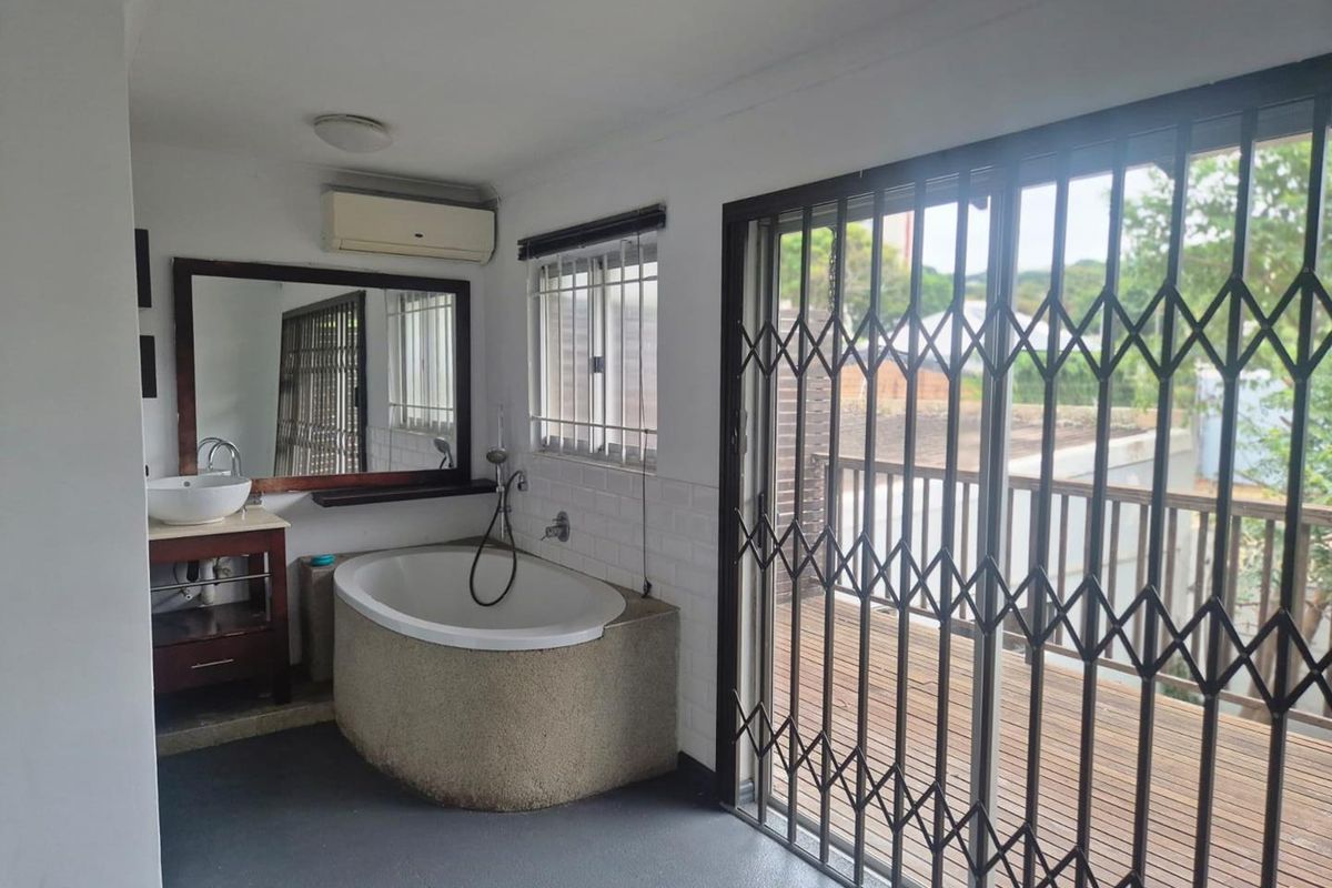 Bathroom featuring a built-in bathtub, vanity with vessel sink, wall-mounted air conditioning unit, and sliding security gate leading to an outdoor balcony.