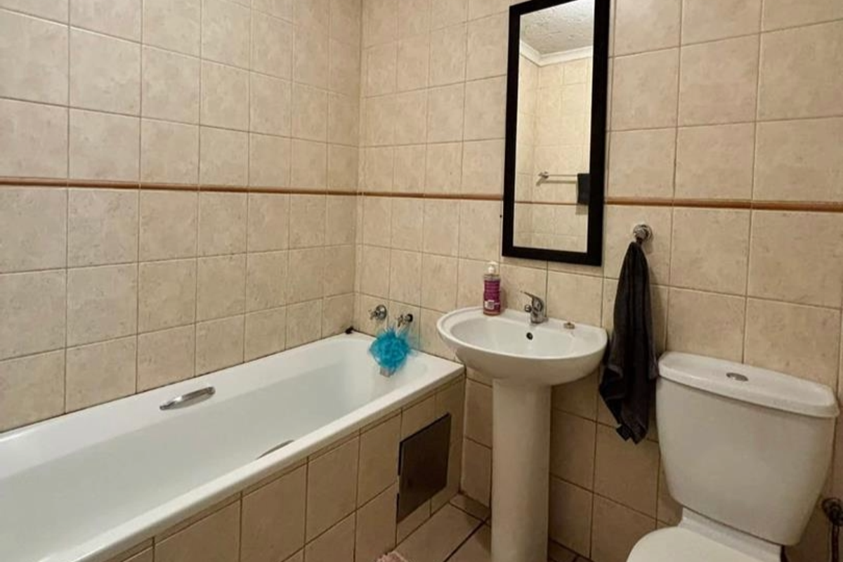 A functional bathroom featuring a tiled bathtub, pedestal sink, and toilet with neutral wall tiling.