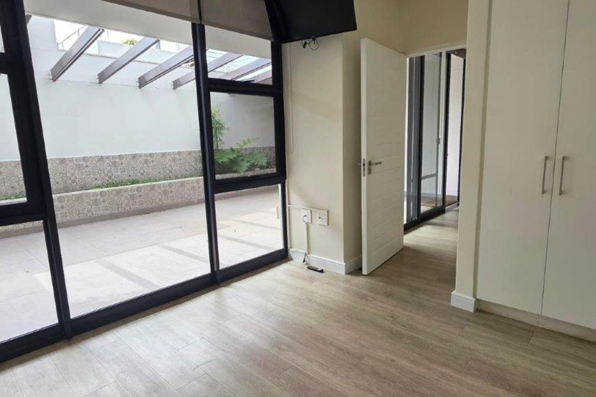 Bright bedroom featuring built-in cupboards, modern laminate flooring, and large sliding doors opening onto a private tiled patio with a pergola.