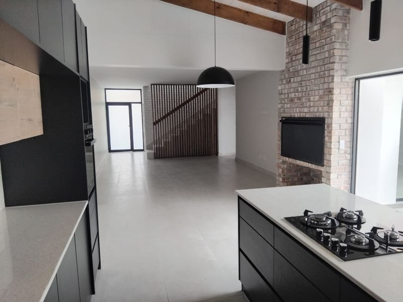 Modern open-plan living area featuring a sleek kitchen with gas hob, exposed timber beams, and a striking brick fireplace, creating a spacious, contemporary atmosphere.