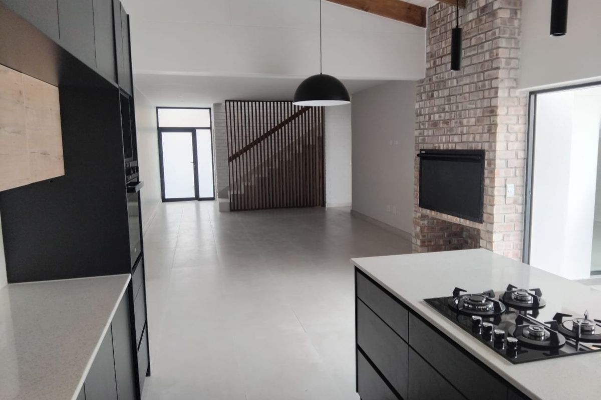 Modern open-plan living area featuring a sleek kitchen with gas hob, exposed timber beams, and a striking brick fireplace, creating a spacious, contemporary atmosphere.