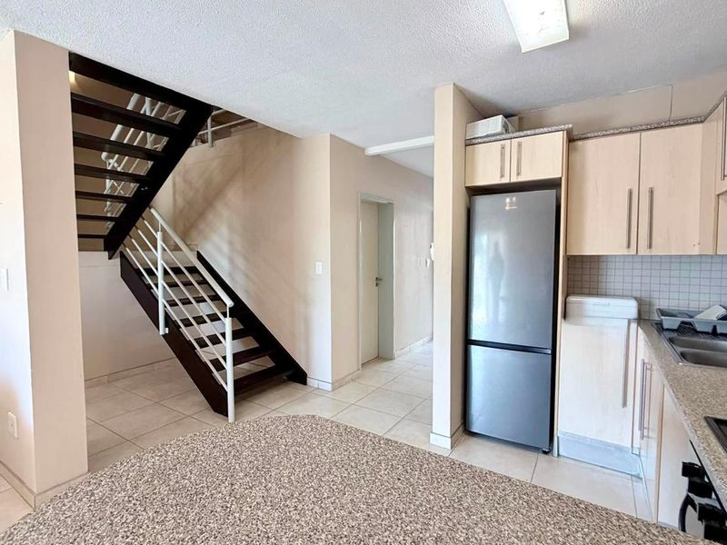 Open plan kitchen area featuring granite countertops, light wood cabinetry, and a staircase leading to the upper level with tiled flooring throughout.