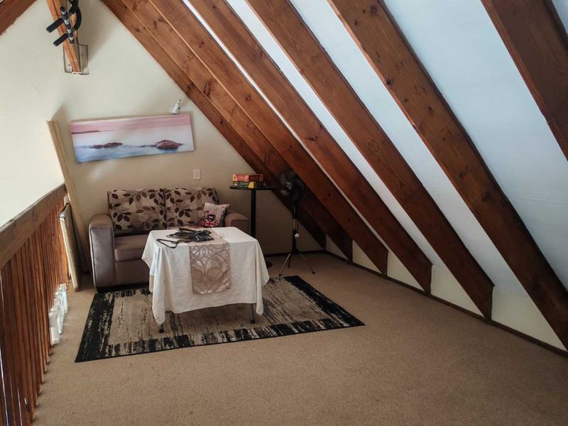 A cozy loft-style living area featuring exposed timber rafters, a wooden balustrade, and carpeted flooring, creating a warm and inviting atmosphere.