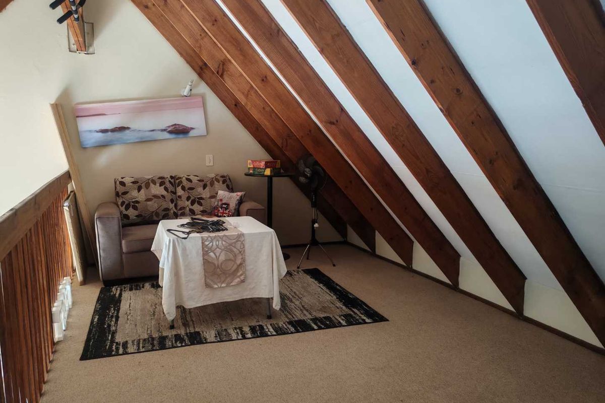 A cozy loft-style living area featuring exposed timber rafters, a wooden balustrade, and carpeted flooring, creating a warm and inviting atmosphere.