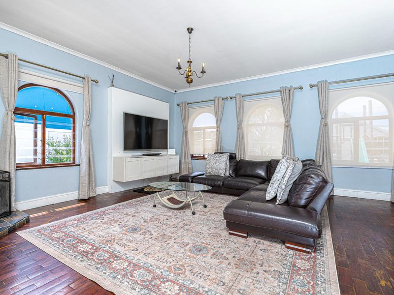 Spacious living room featuring hardwood flooring, arched windows, a built-in media console, and a fireplace with a stone hearth.