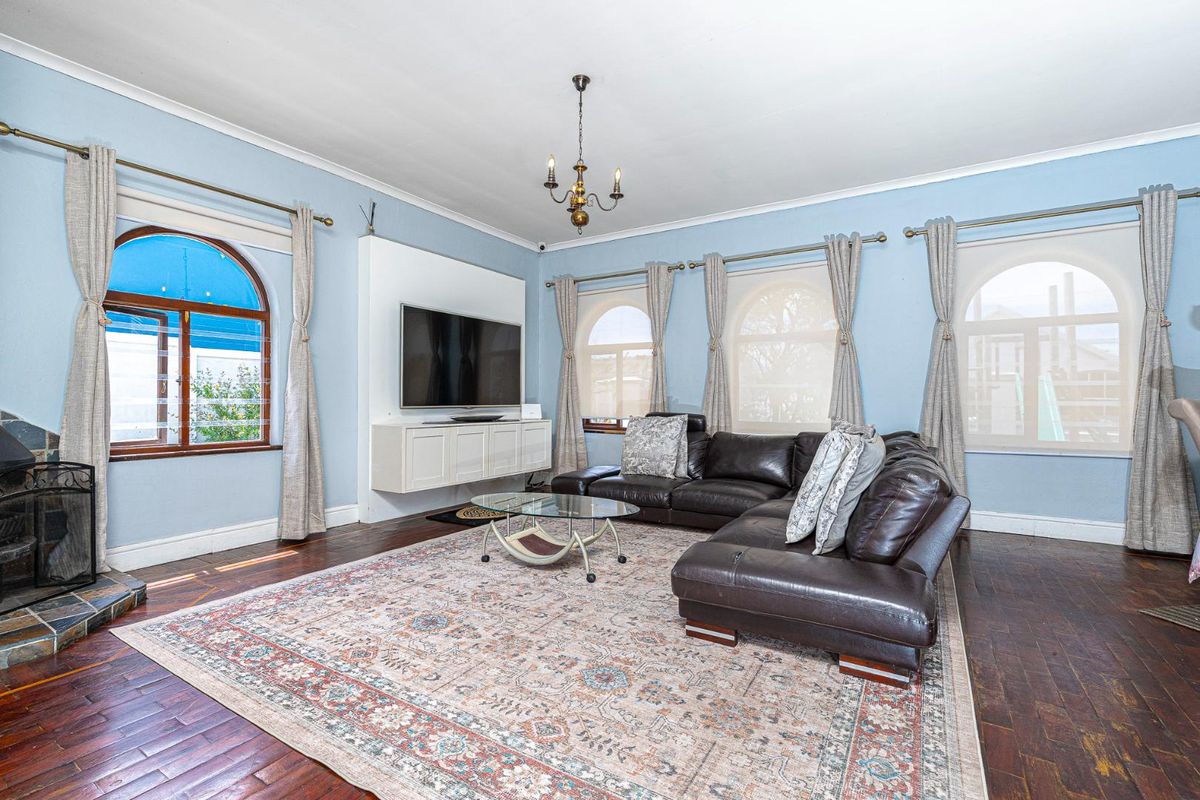 Spacious living room featuring hardwood flooring, arched windows, a built-in media console, and a fireplace with a stone hearth.