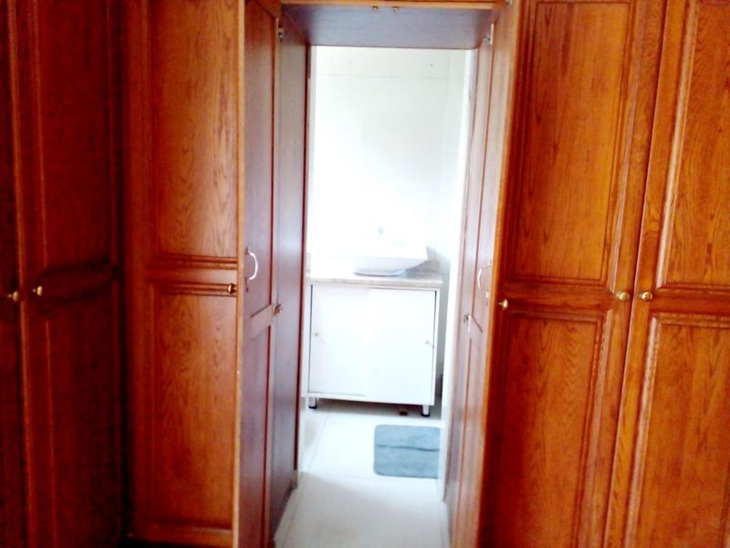 A view through a doorway flanked by built-in wooden cupboards leading into a bathroom featuring a vanity cabinet and basin.