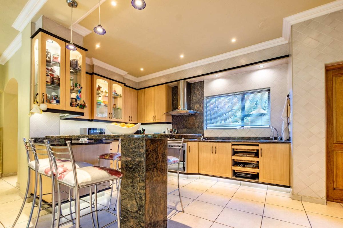A well-appointed kitchen featuring light wood cabinetry, granite countertops, a breakfast bar, stainless steel extractor fan, and tiled flooring with recessed lighting.