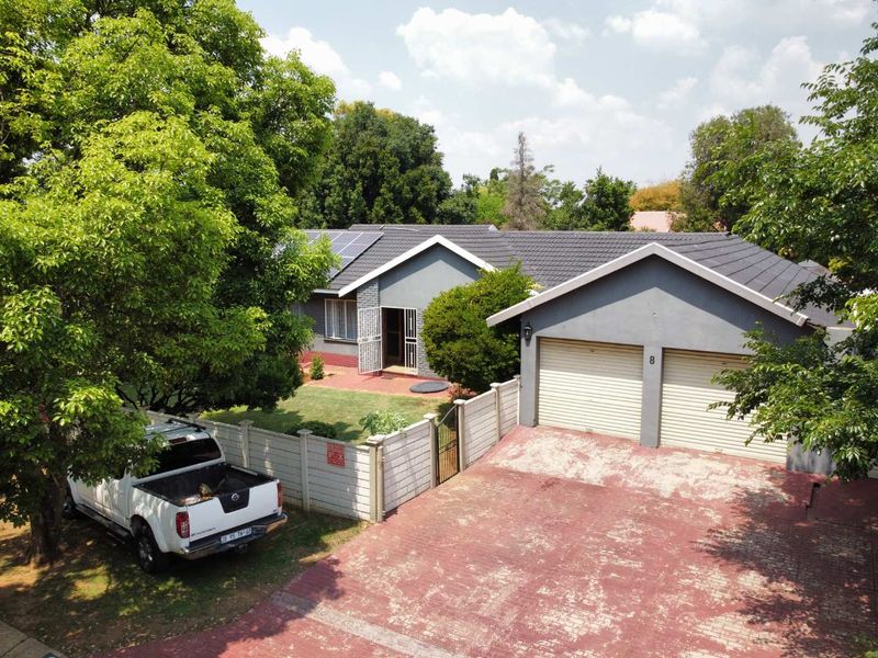 Aerial view of a residential property featuring a double garage, tiled roof with solar panels, and a paved driveway set within a landscaped garden.