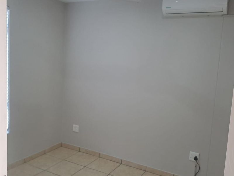 A clean, empty bedroom featuring tiled flooring, a ceiling fan, and a wall-mounted split-system air conditioning unit.