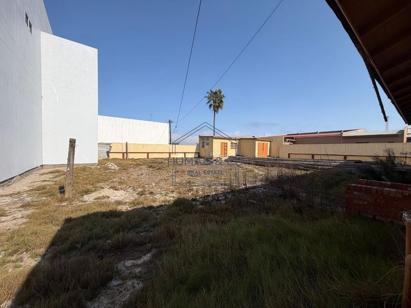 Rear yard area featuring a boundary wall and a small outbuilding, currently requiring significant landscaping and ground maintenance.