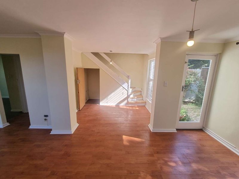 An open-plan living area featuring laminate flooring, a staircase with under-stair storage, and a glass door providing access to the exterior.