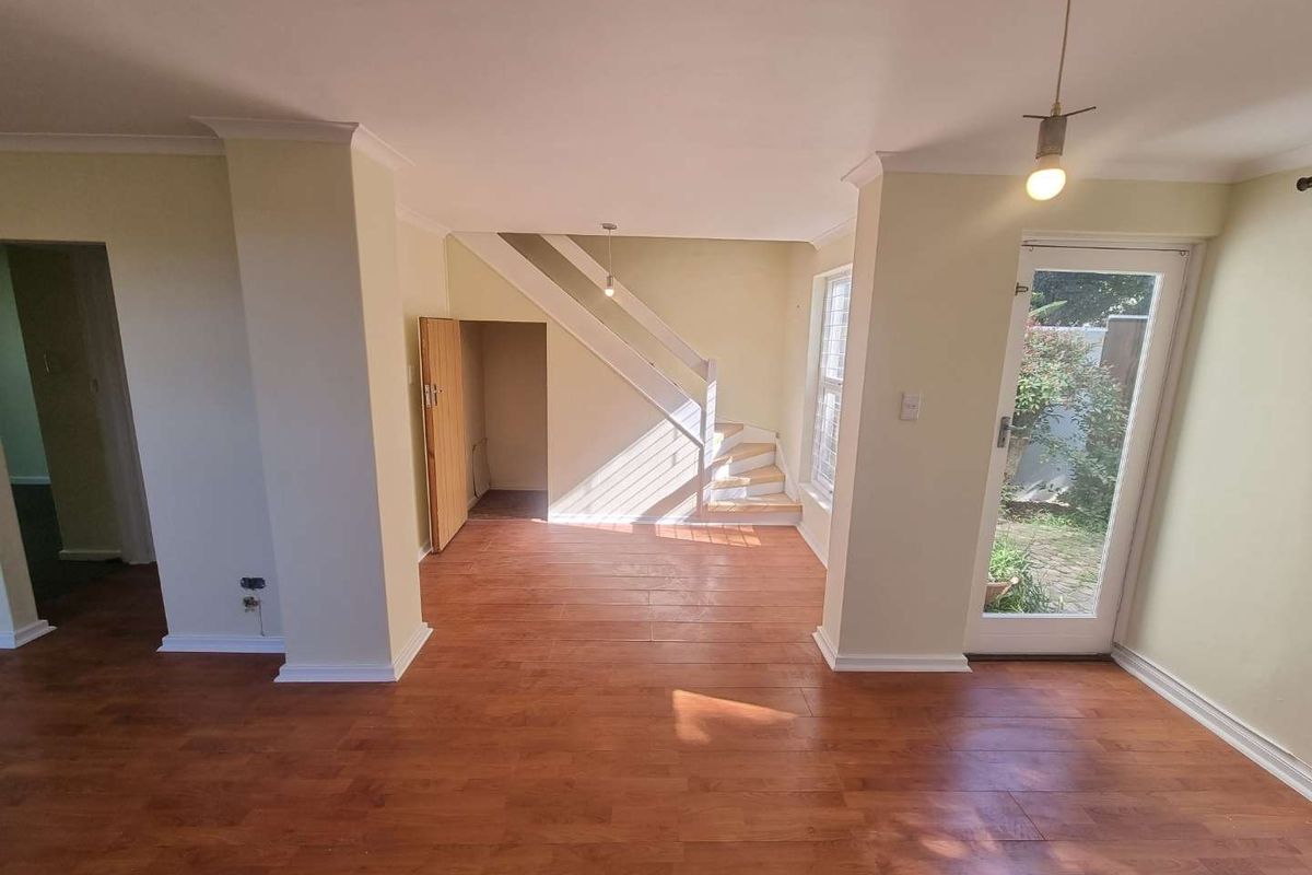 An open-plan living area featuring laminate flooring, a staircase with under-stair storage, and a glass door providing access to the exterior.