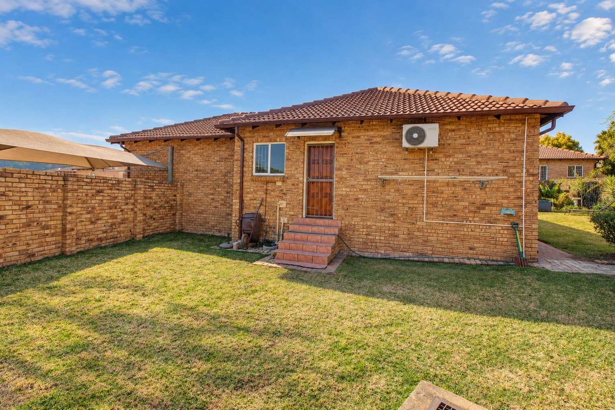 Rear view of a townhouse featuring a face brick exterior, tiled roof, private lawn, and a secure entrance with tiled steps.