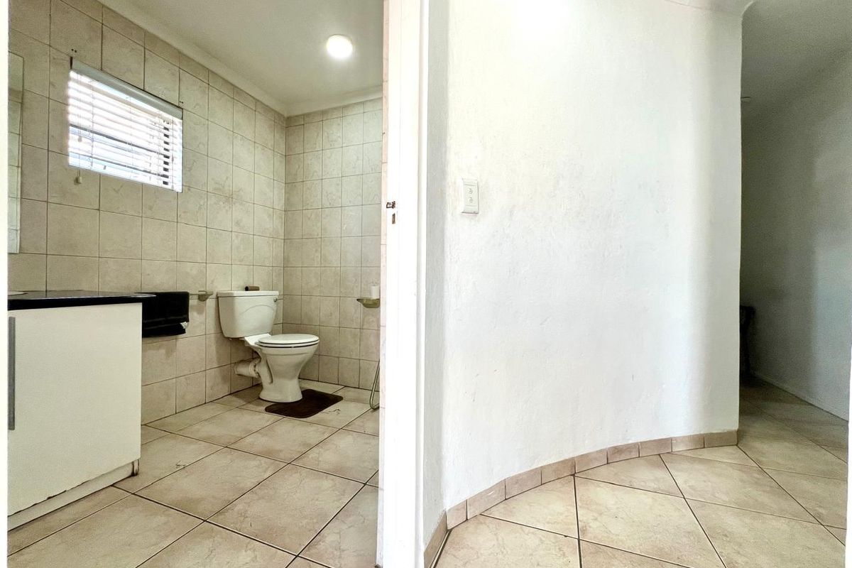 A functional bathroom featuring tiled walls and flooring, a built-in vanity, and a standard toilet, accessible from a tiled hallway.
