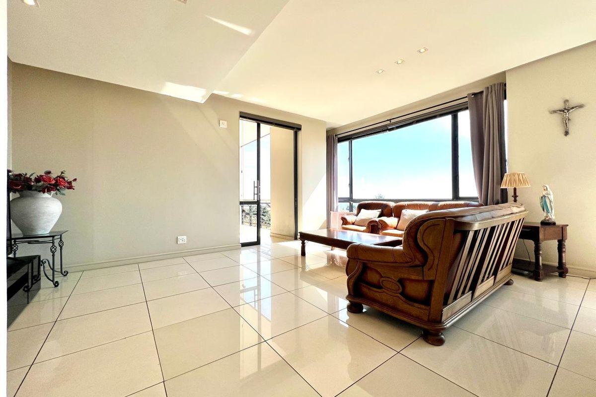 Spacious living room featuring large format floor tiles, recessed lighting, and expansive windows providing natural light and access to an adjoining balcony.