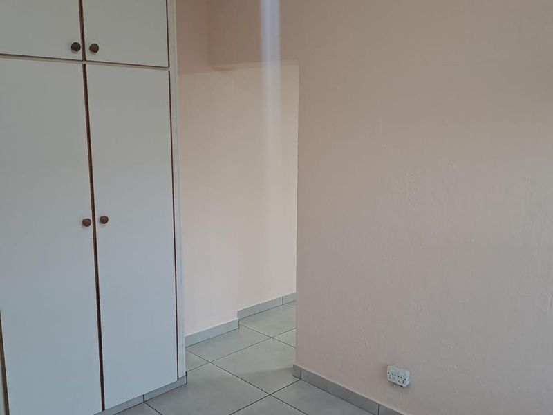 A clean, empty bedroom featuring neutral wall paint, tiled flooring, and built-in storage cupboards.