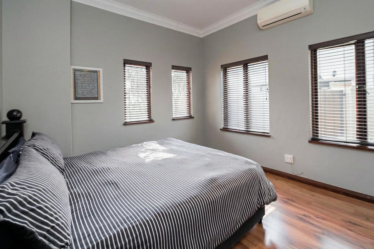 A well-maintained bedroom featuring wood-look flooring, multiple windows with fitted blinds, and a wall-mounted air conditioning unit.