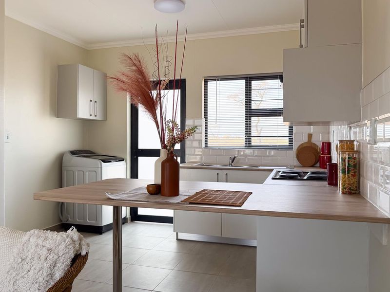 A bright, modern kitchen featuring white cabinetry, a wood-look breakfast bar, subway tile backsplash, and integrated hob with extractor fan.