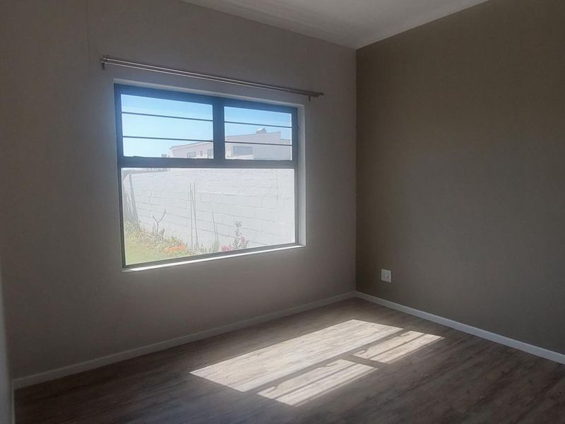 A bright, empty bedroom featuring modern laminate flooring, neutral wall tones, and a window fitted with security bars.