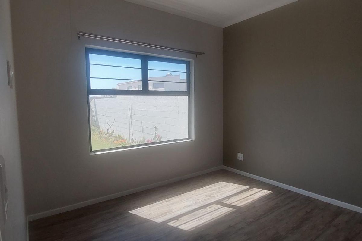 A bright, empty bedroom featuring modern laminate flooring, neutral wall tones, and a window fitted with security bars.