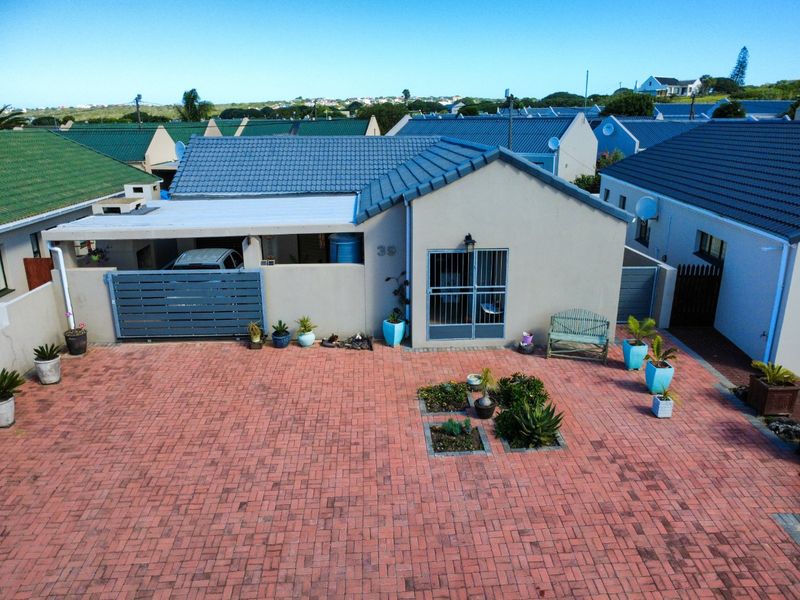 Aerial view of the front exterior featuring a paved driveway, covered carport, and a well-maintained facade with secure entrance gate.