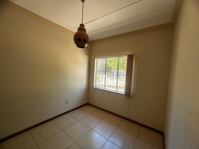 A clean, empty bedroom featuring neutral tiled flooring, security bars on the window, and decorative ceiling cornicing.