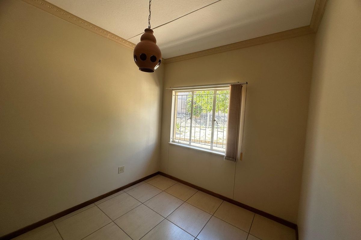 A clean, empty bedroom featuring neutral tiled flooring, security bars on the window, and decorative ceiling cornicing.