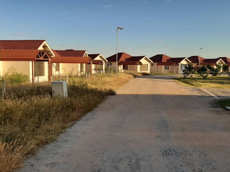 A street view of a residential development featuring multiple detached houses with tiled roofs and an unpaved access road.